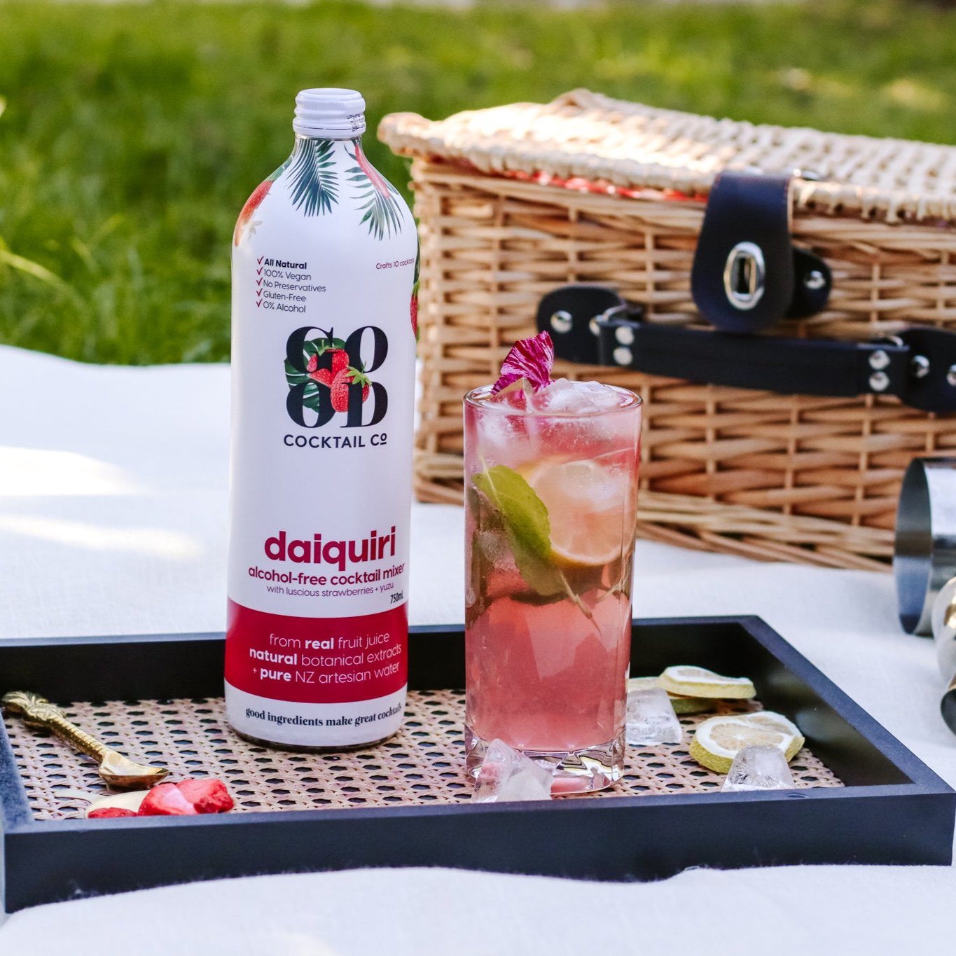 Daiquiri cocktail mixer in bottle on tray in picnic next to glass of cocktail 